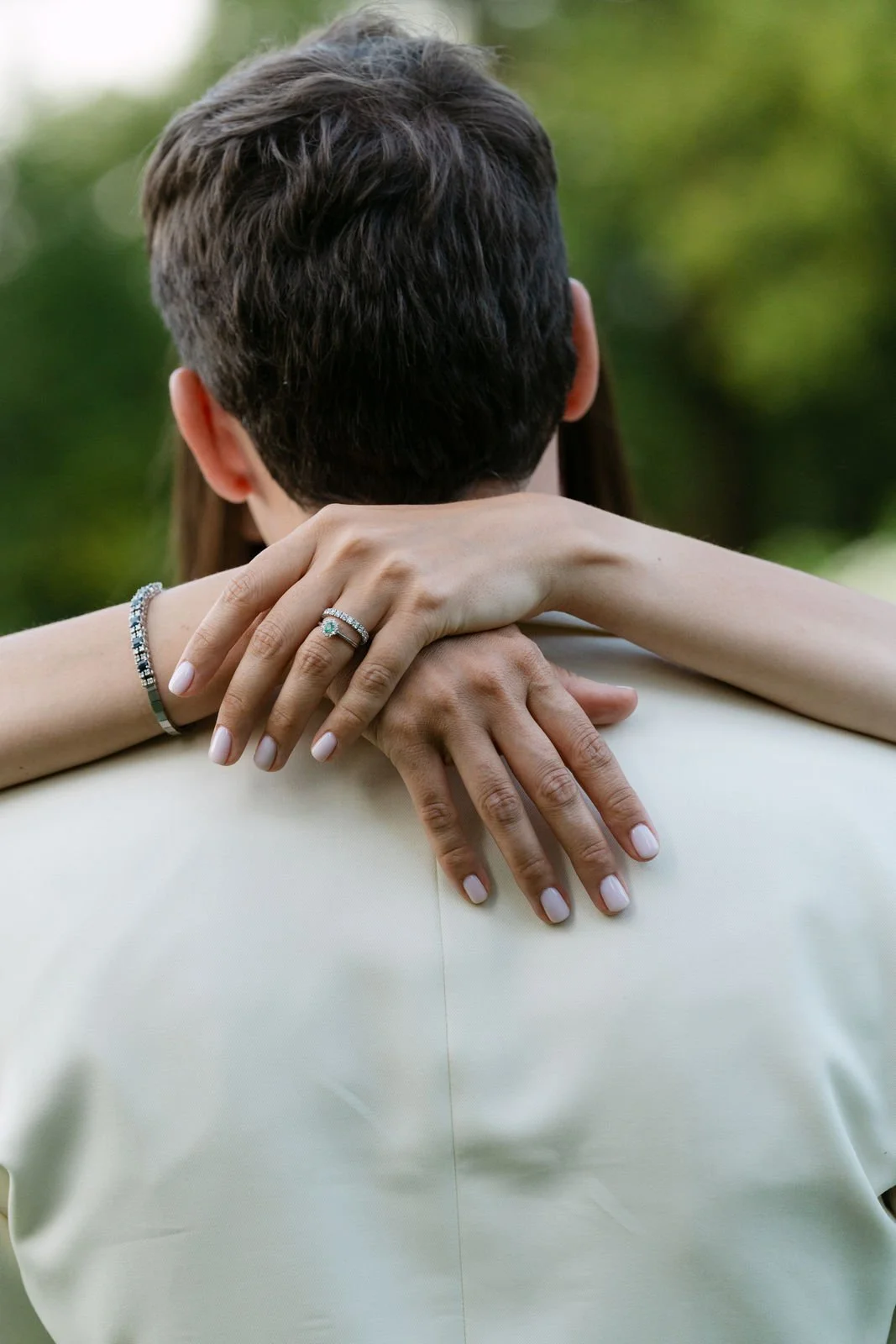 Ein Paar umarmt sich im Freien, die Hände des Paares sind sichtbar, das weibliche Paar trägt Ringe an den Fingern, die sich um den Hals des männlichen Partners wickeln, beide tragen Schmuck, im Hintergrund sind bunte Blätter