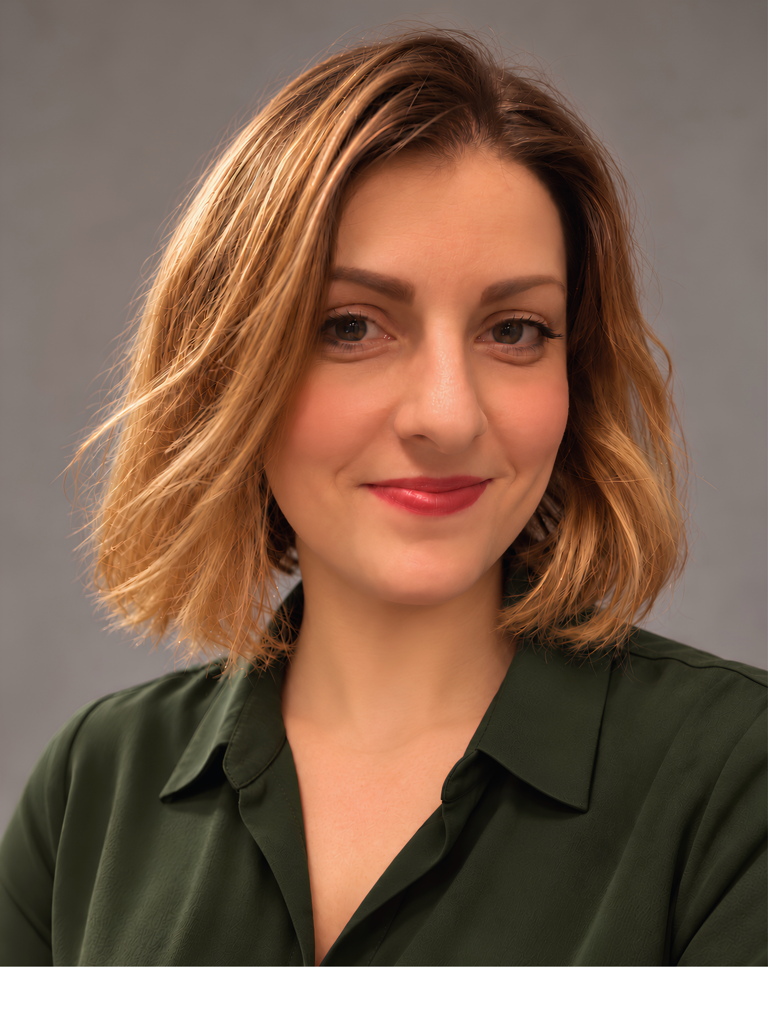 Nahaufnahme einer lächelnden Frau mit braunen Haaren, die einen schwarzen Blazer trägt, vor einem neutralgrauen Hintergrund.