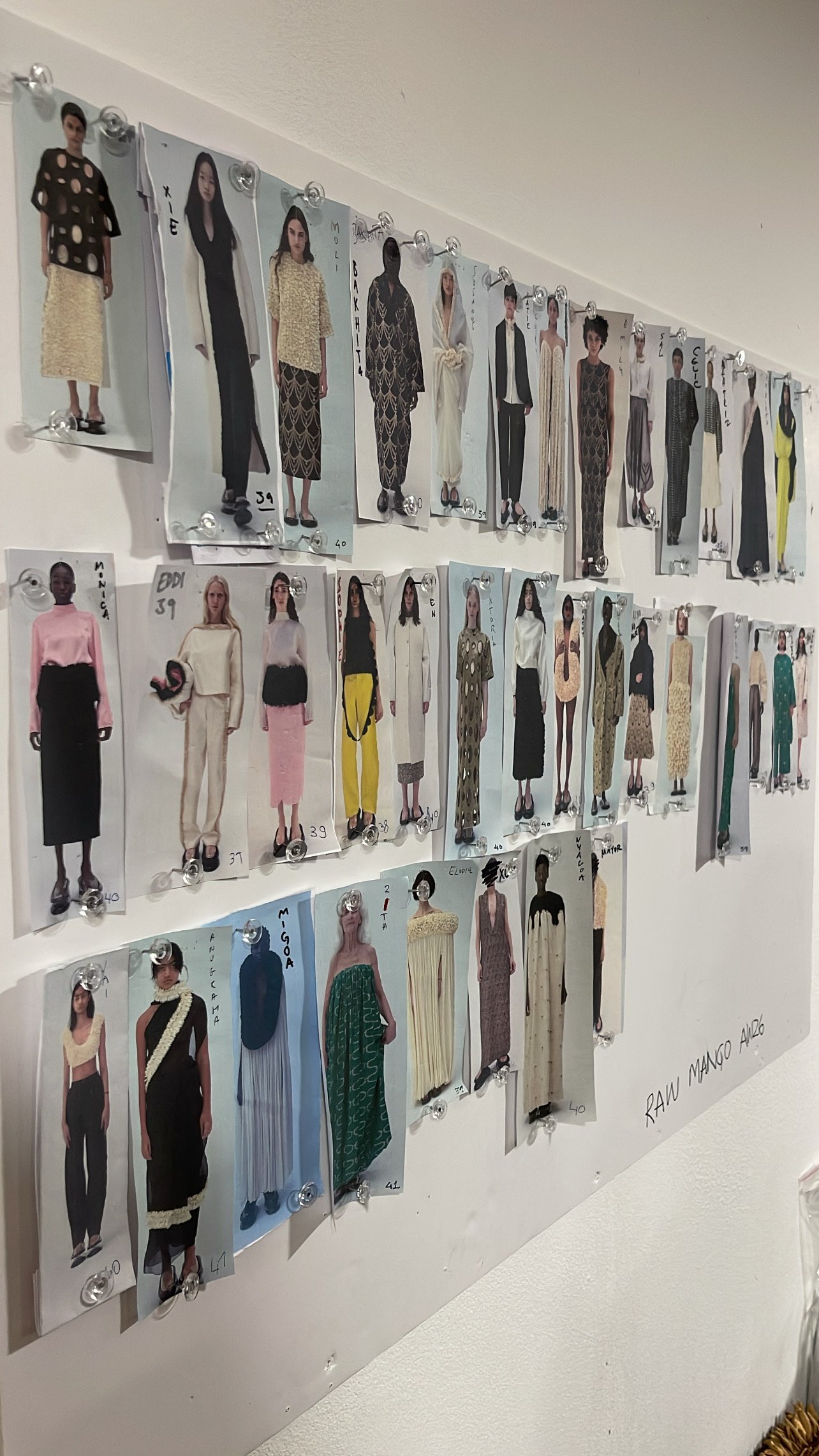 A wall display of fashion sketches pinned with clear clips, showcasing various clothing designs and models.