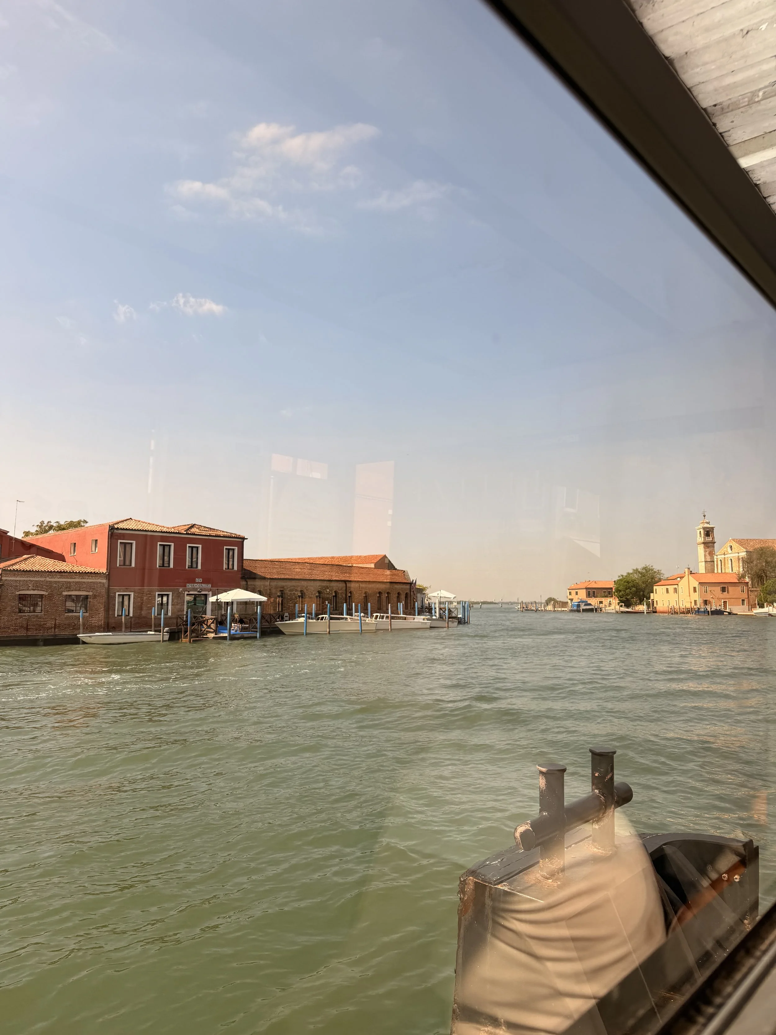 A view of a canal with colorful buildings and boats, taken from inside a boat, with a part of the boat's window and boat equipment visible in the foreground.