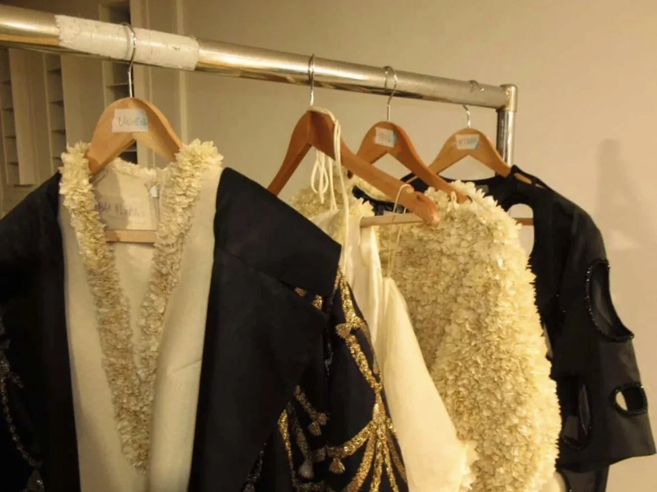 Clothes hanging on a metal clothing rack, including formal and decorative dresses with floral and embellishment details.