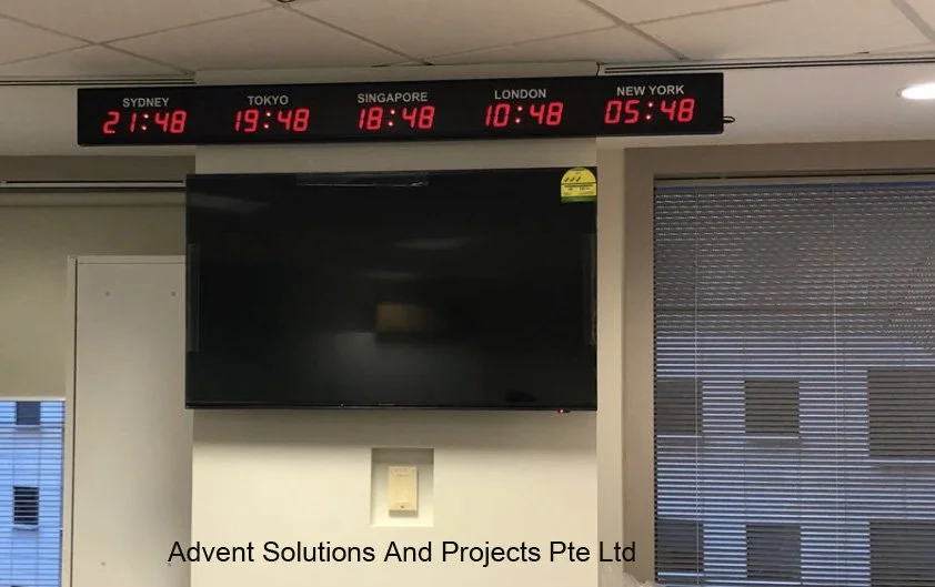 Digital world clock showing times for Sydney, Tokyo, Singapore, London, and New York, and a blank television screen below, in an office room.
