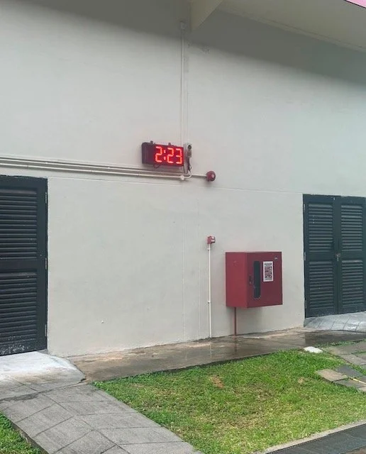 Exterior wall with digital clock showing 2:23, fire alarm box, and two black vents.