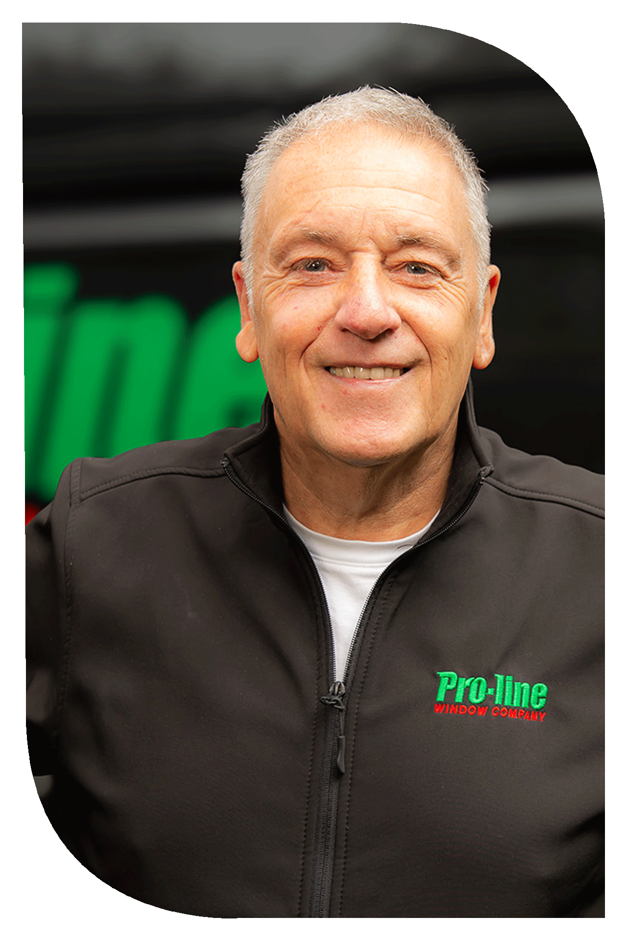 A smiling middle-aged man with gray hair, wearing a black jacket with a zipper, featuring a green and red logo that reads "Pro-line Window Company."