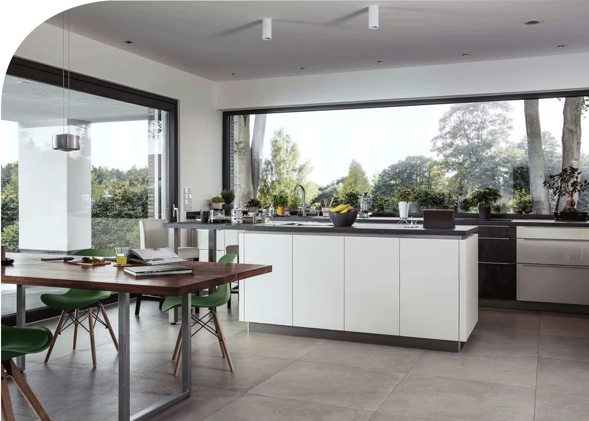 Modern kitchen with large window, white cabinets, black countertop, and a wooden dining table with green chairs.