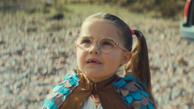 A young girl with glasses and pigtails looking up outdoors in a rocky area.