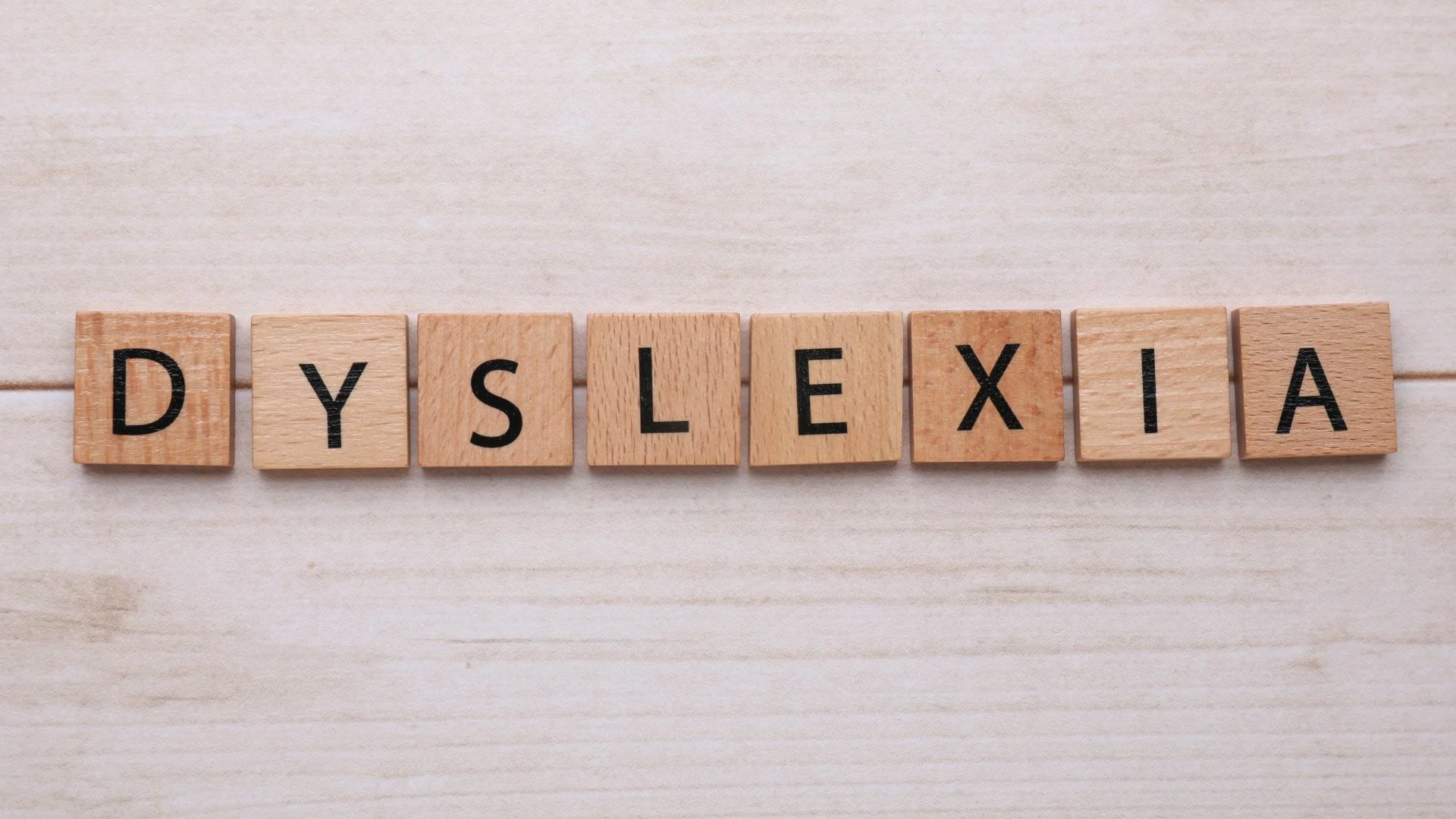 Wooden letter tiles spelling “DYSLEXIA” on a light wood surface