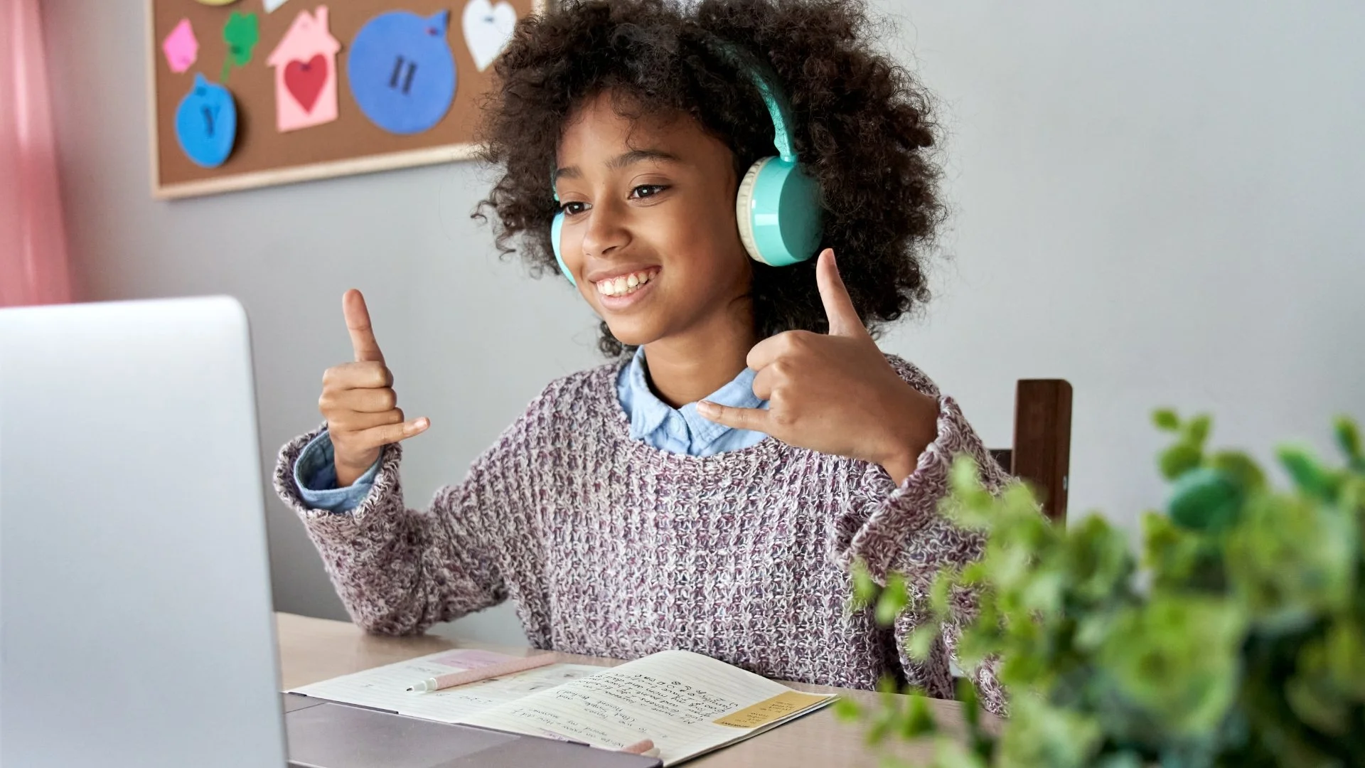 Smiling child wearing turquoise headphones and making hand gestures while studying at a laptop