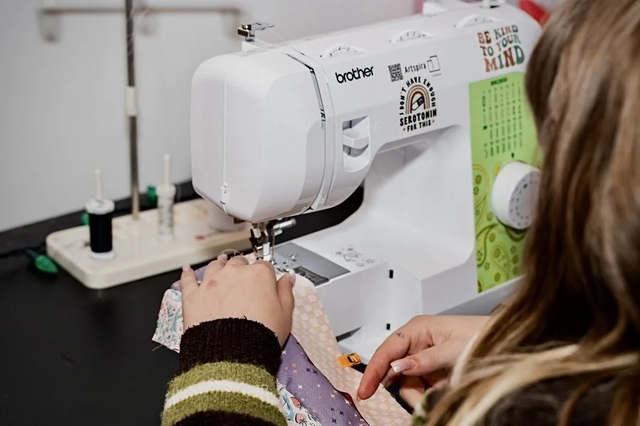 Person sewing fabric using a Brother sewing machine in a craft room.
