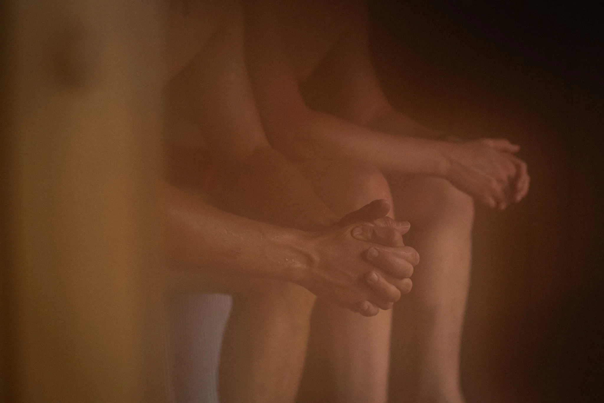 People sitting on a sauna bench. Sweating, hands in their lab. The image is blurry and warm-toned.
