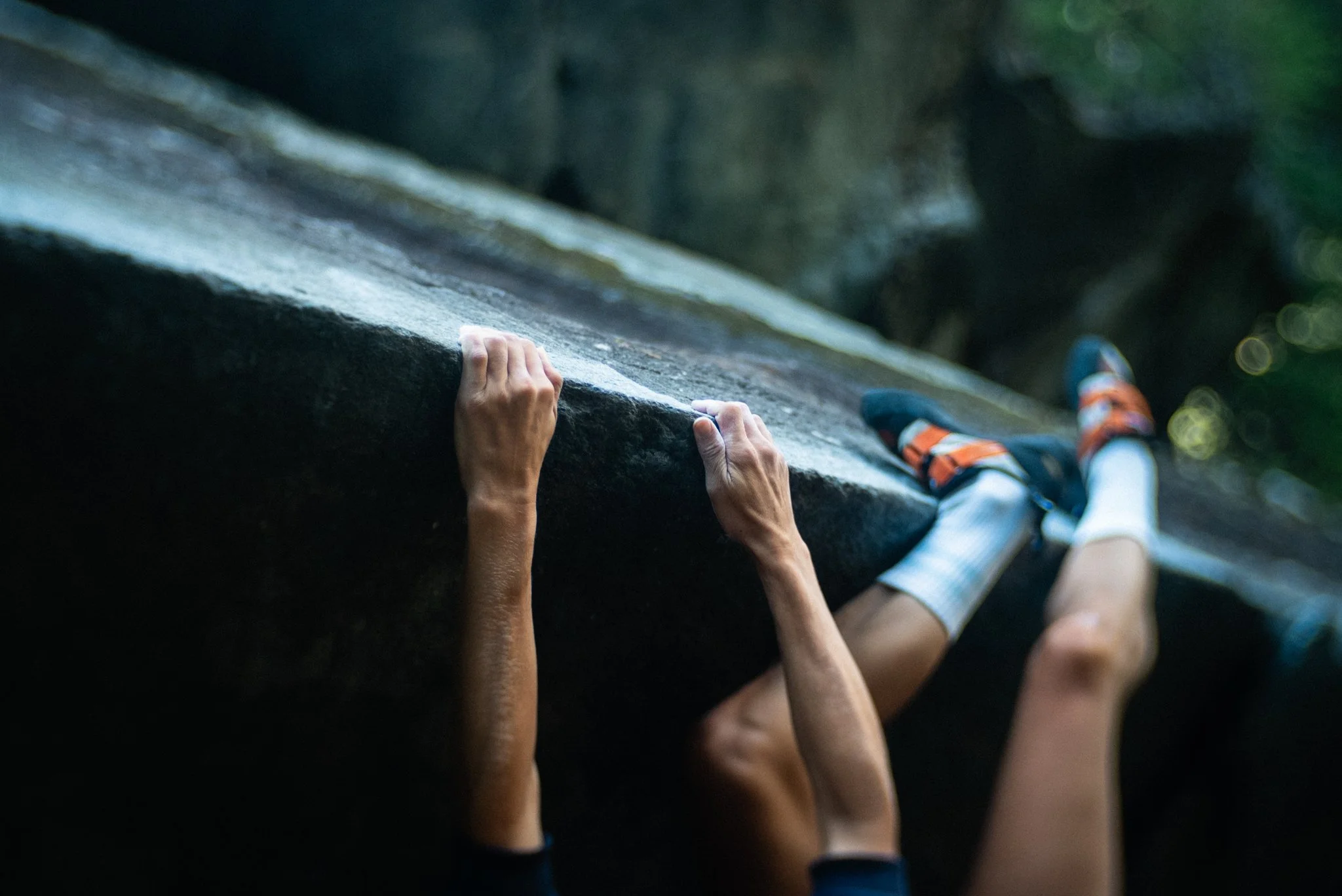 Close-up of a person rock climbing outdoors, showing hands gripping a rock wall and legs in climbing shoes.