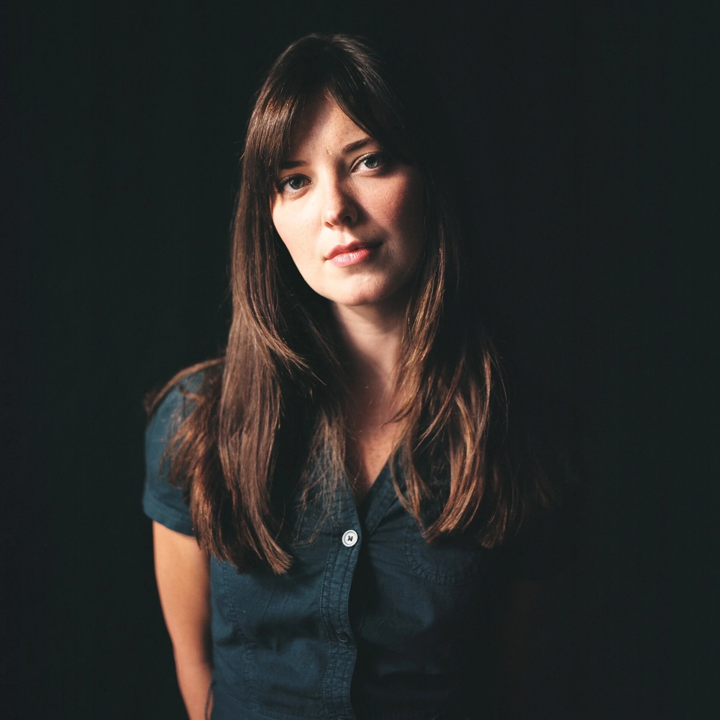 The author Jenn Thorne - a close-up of a young woman with long brown hair, wearing a dark denim shirt, looking directly at the camera with a neutral expression against a dark background.