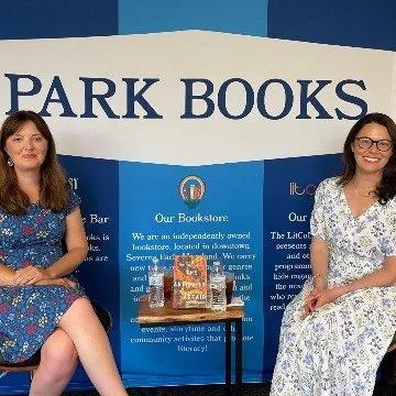 Two women sitting on chairs in front of a blue and white banner that reads "Park Books" at a bookstore event.
