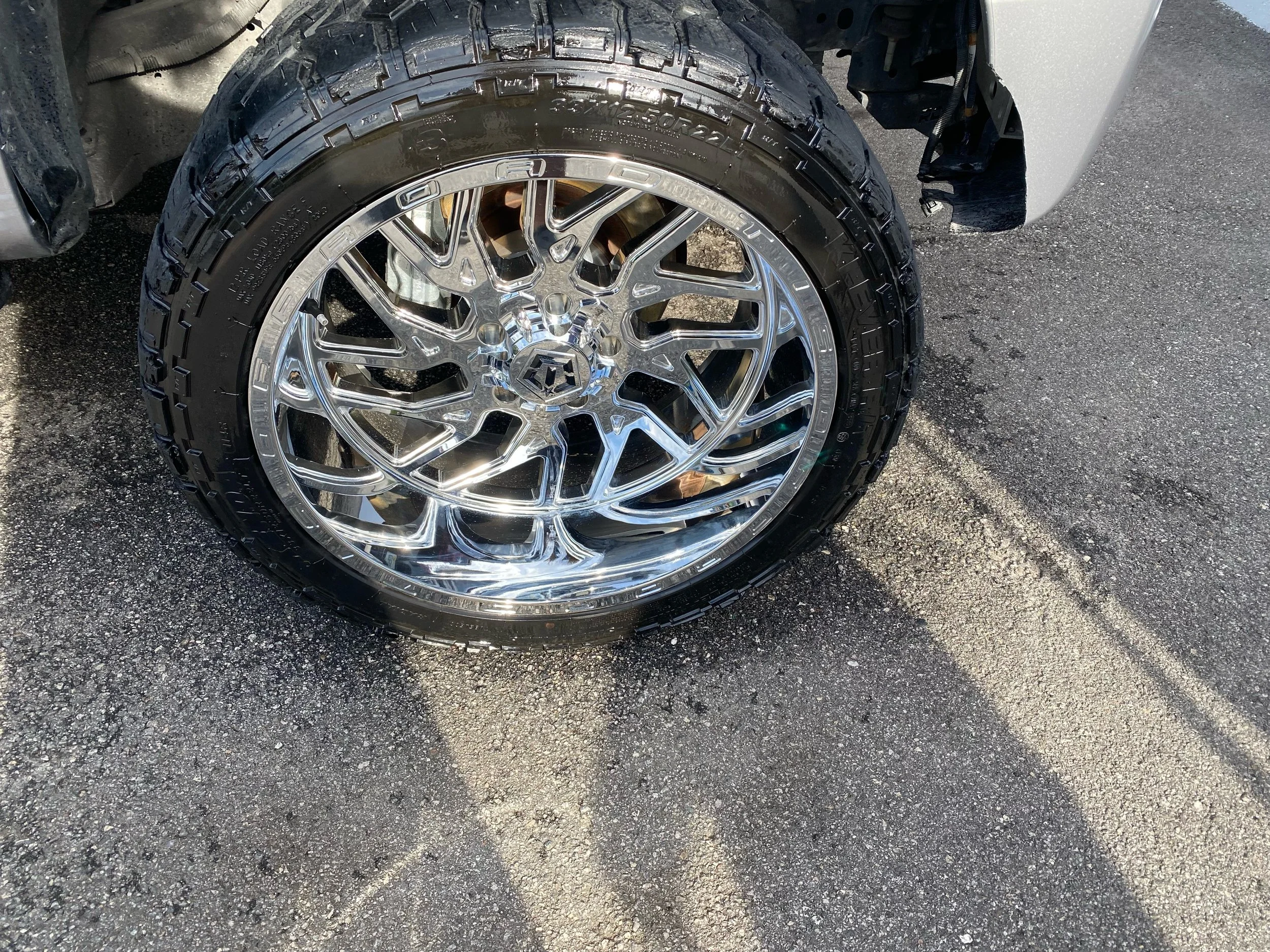 Close-up of a shiny, chrome car wheel with a off-road tire mounted on a black asphalt surface.