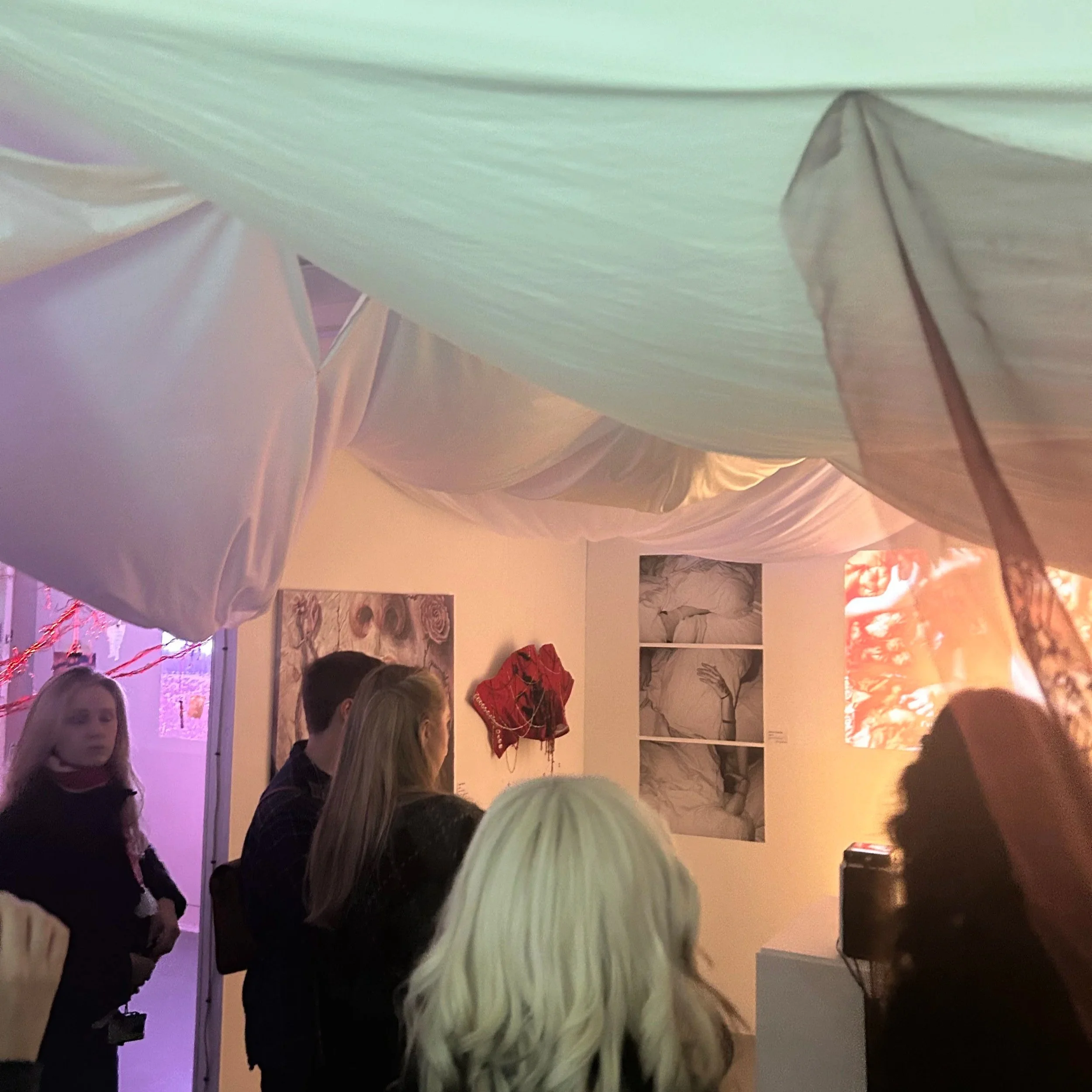 People gathered in an art gallery or museum, looking at various artwork and sculptures displayed on the walls and shelves.