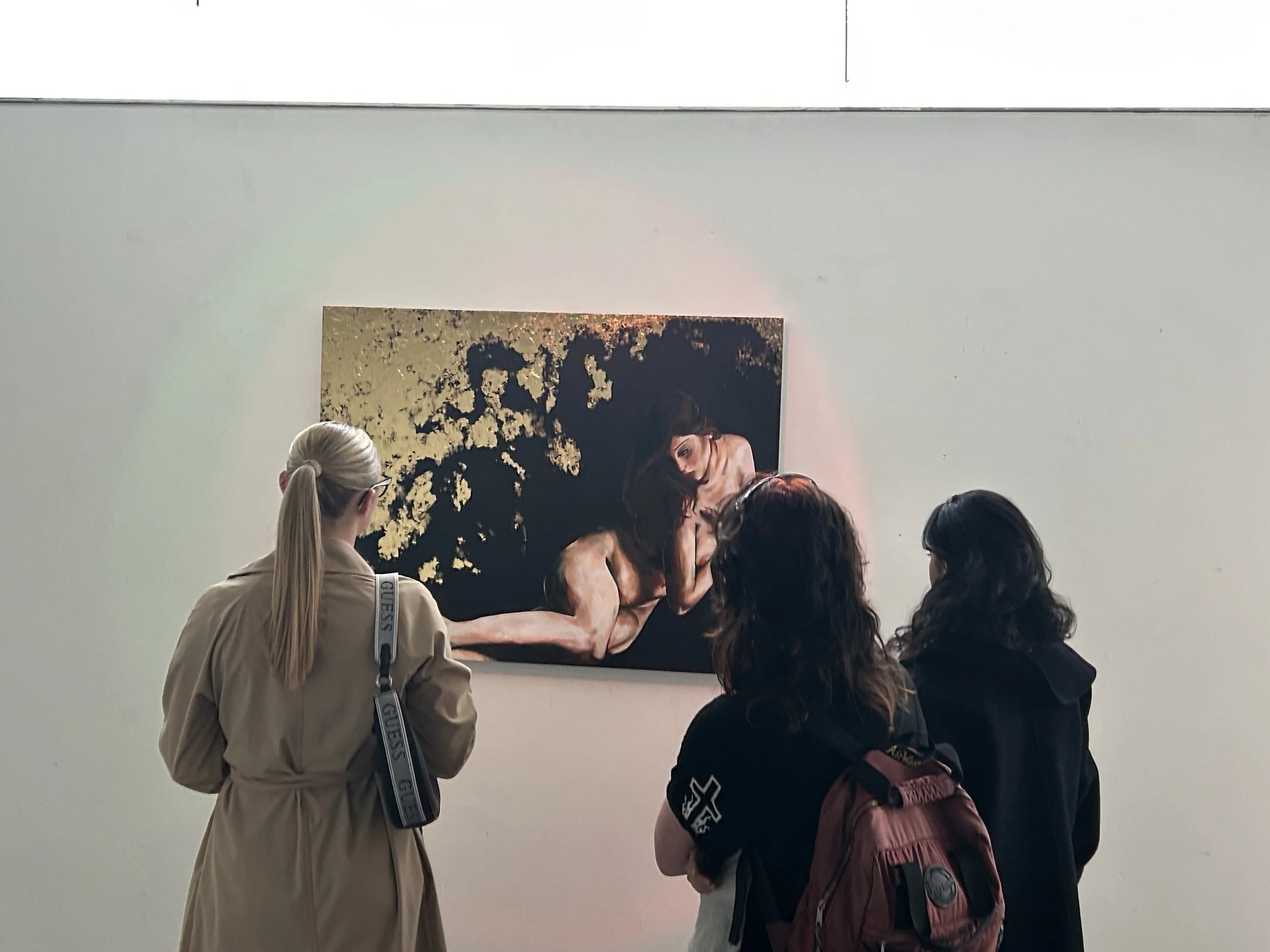 People viewing a portrait painting of a woman with dark hair, set against a dark, textured background, in an art gallery with a white wall.
