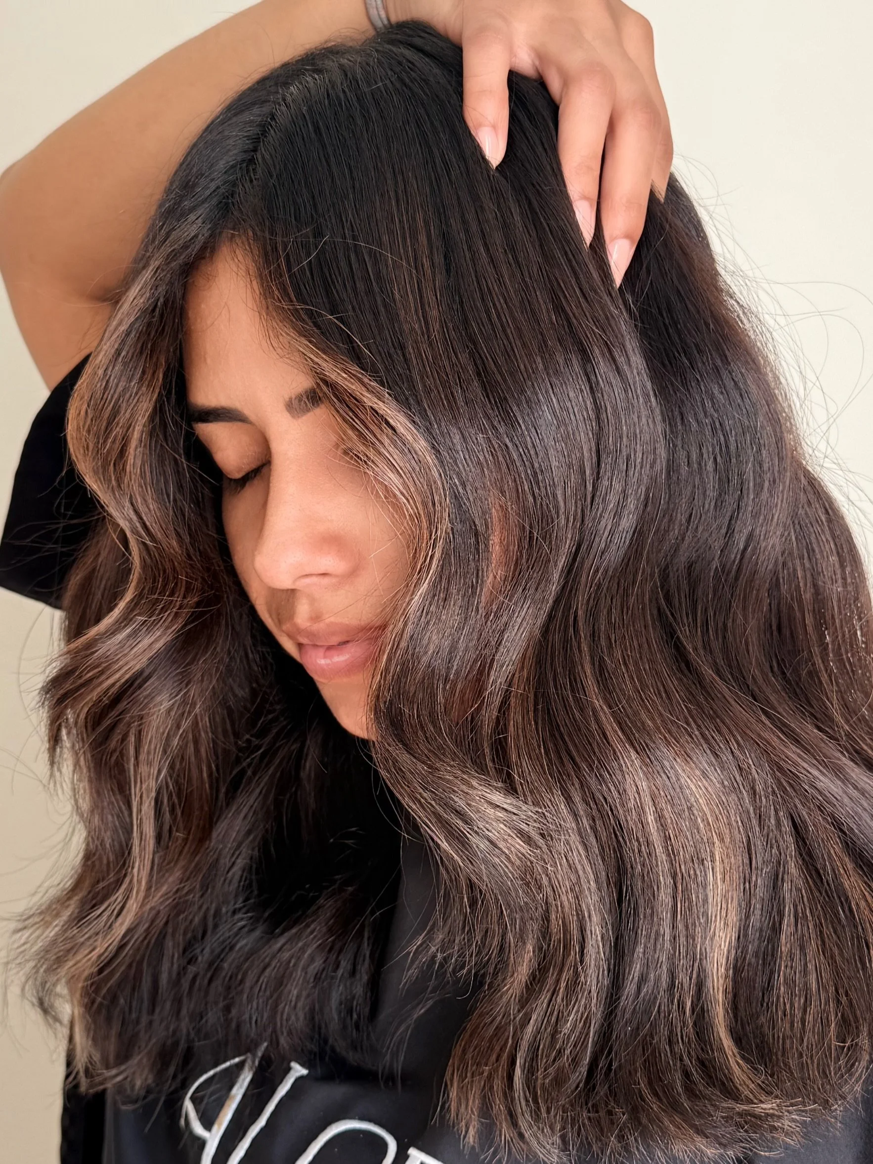 Close-up of a woman with wavy hair with brown highlights for a caramel color balayage. Color, style, and photo done by Melissa Jaramillo at Aloe Studio.