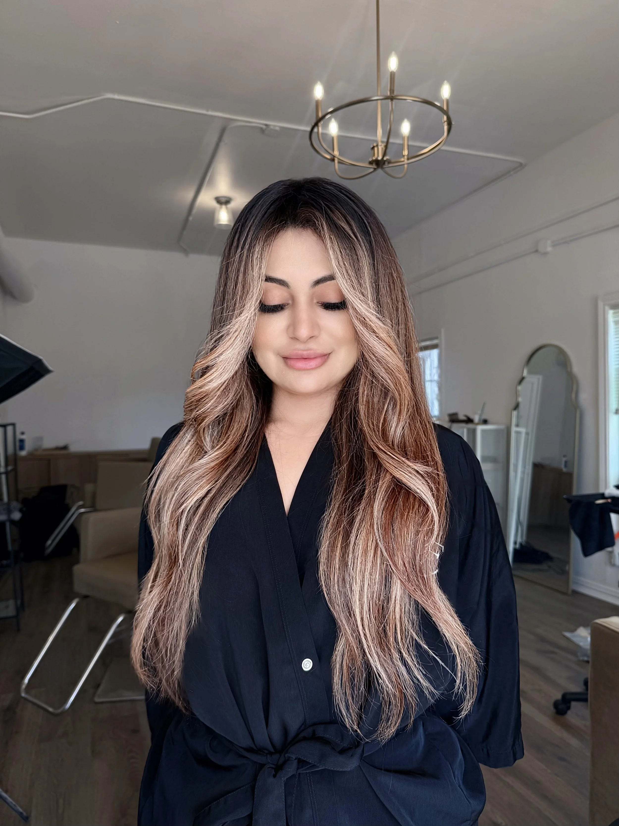 Client in a salon robe showing long dimensional blonde balayage inside Aloe Studio, a luxury Houston salon.