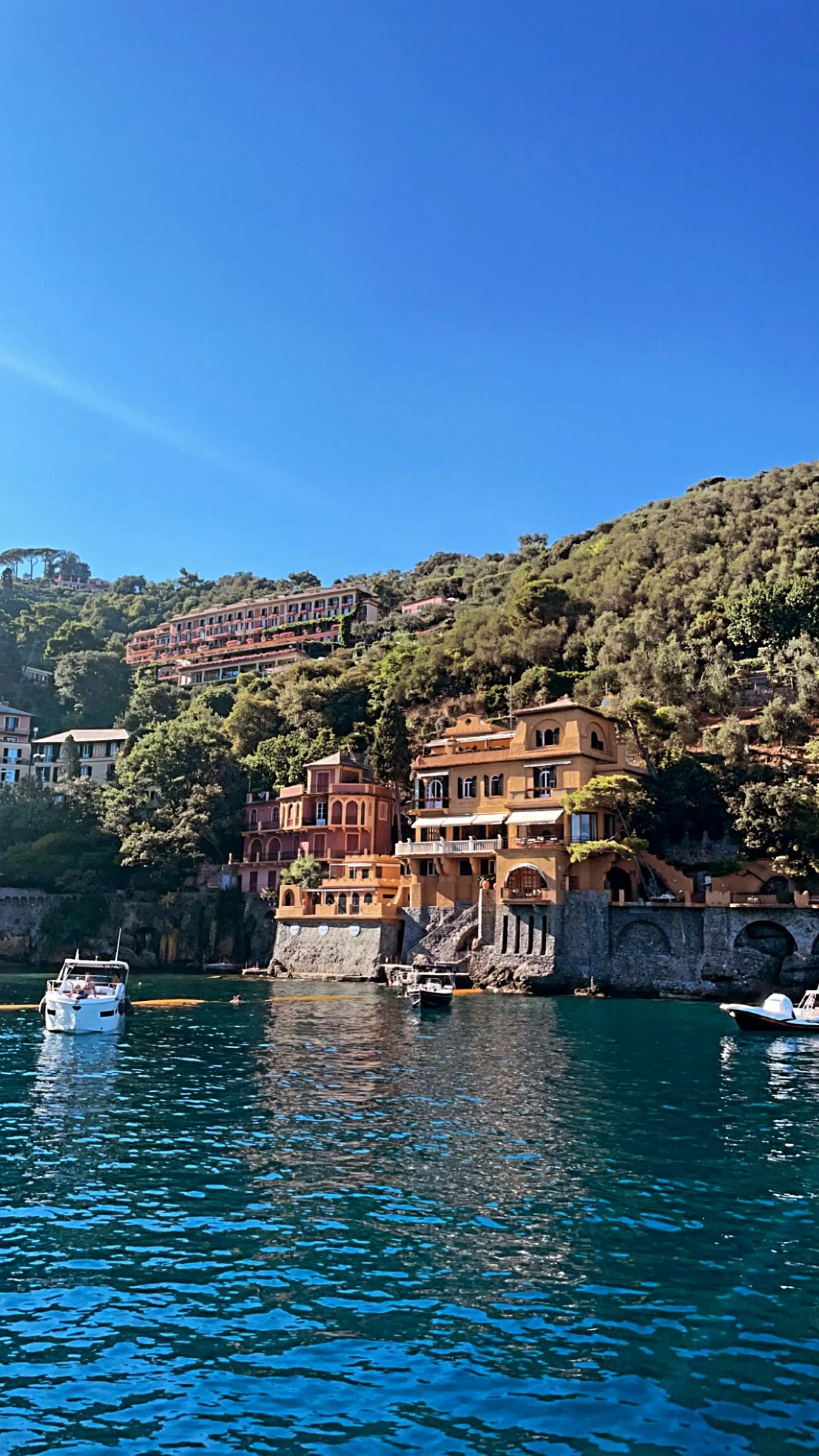Colorful Mediterranean-style buildings on a hillside by the water with boats, under a clear blue sky.
