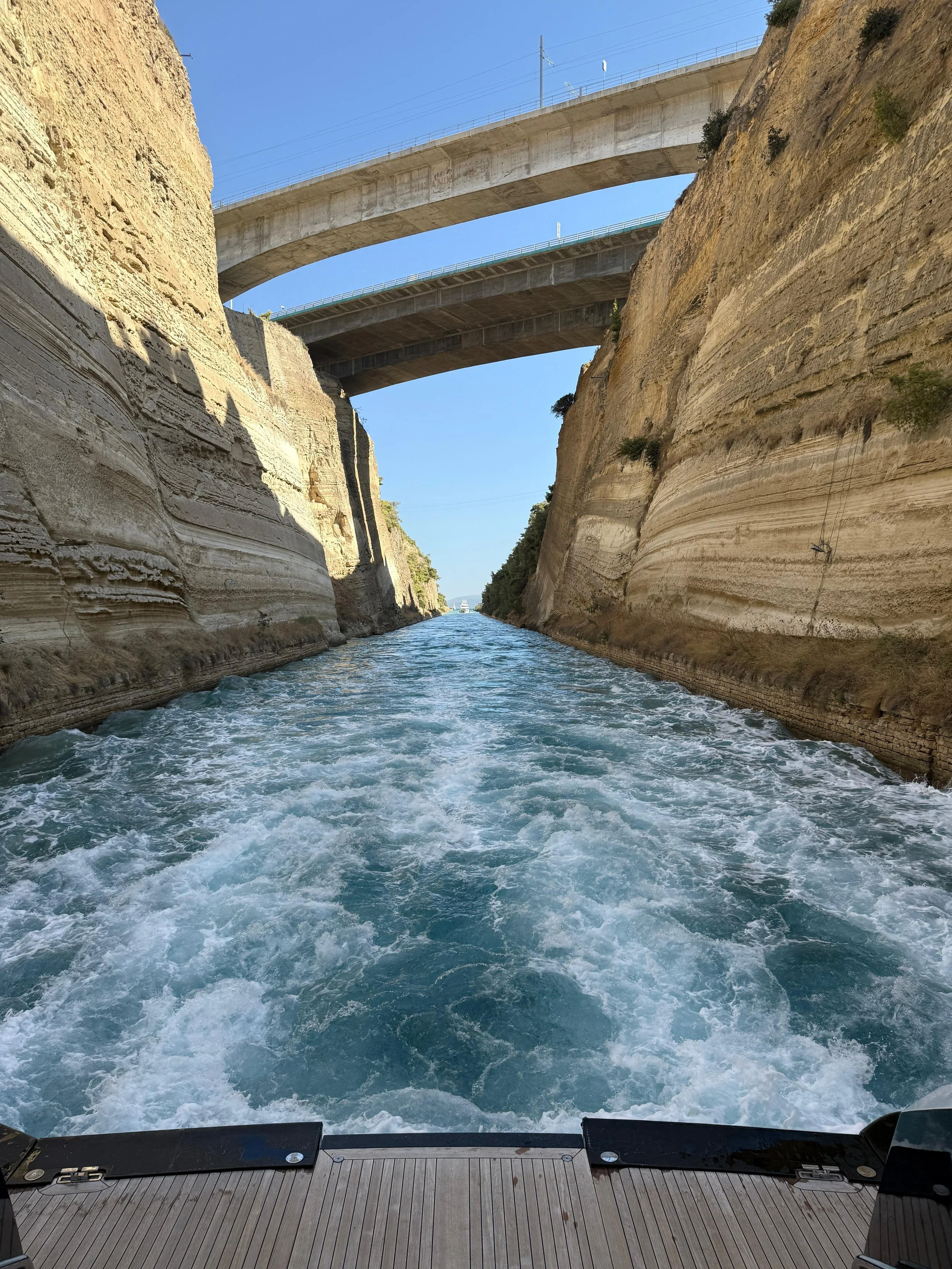 View from a boat on a waterway with high cliffs on either side and bridges overhead, under a clear blue sky.
