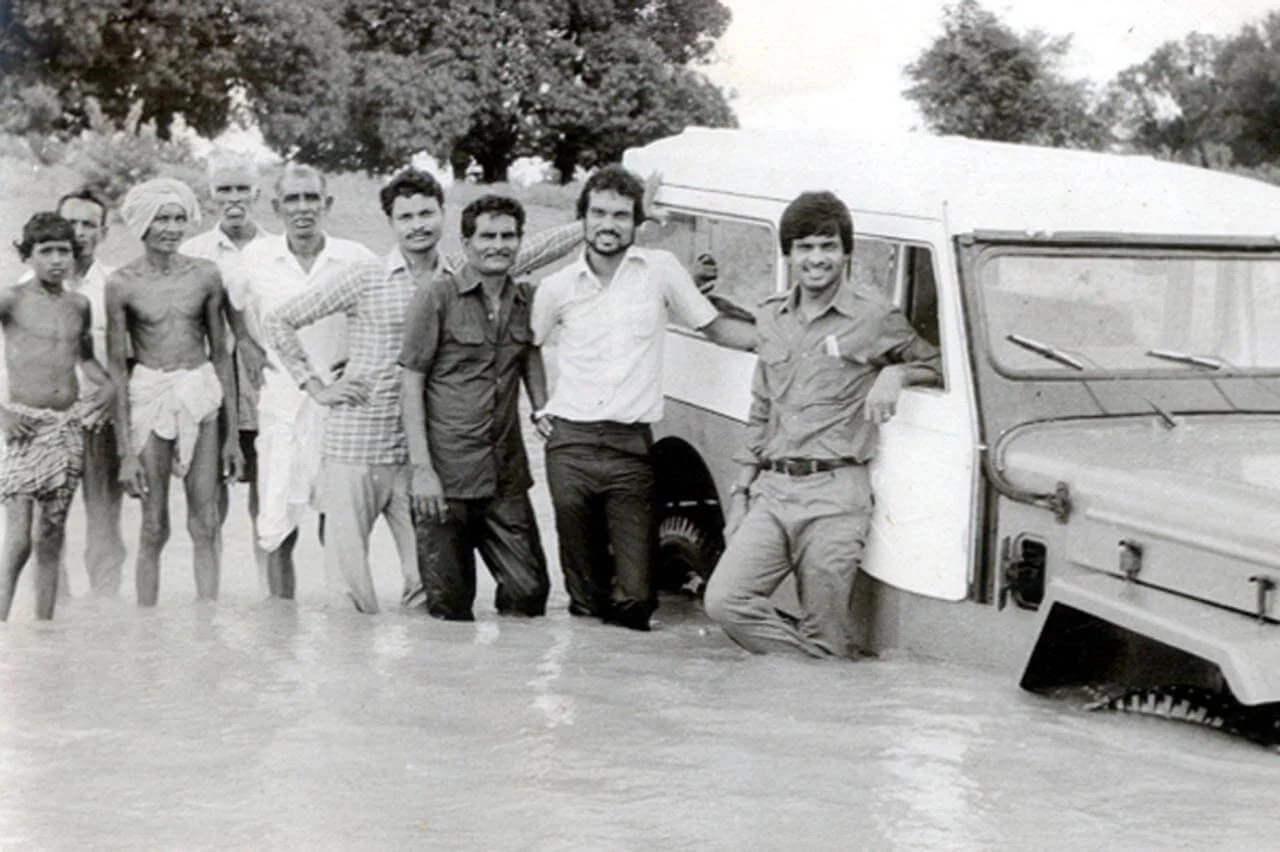 Group of people standing in floodwaters next to a vehicle.