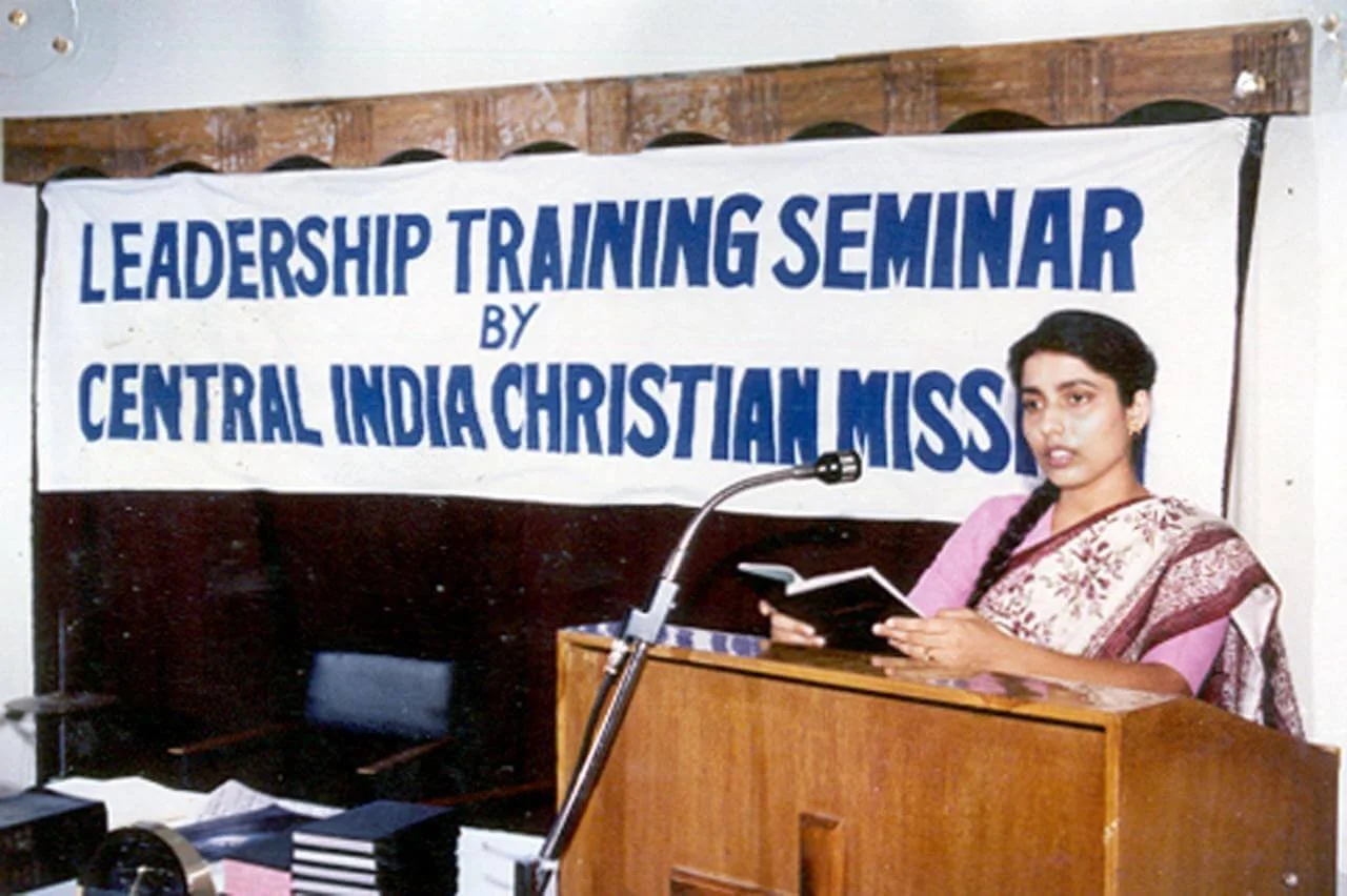 A woman in traditional Indian attire speaking at a leadership training seminar organized by Central India Christian Miss, with a banner behind her.