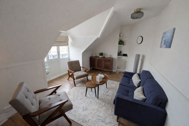 Bright modern therapy room with a navy sofa, two gray armchairs, round coffee tables, area rug, and mid-century wooden cabinet.