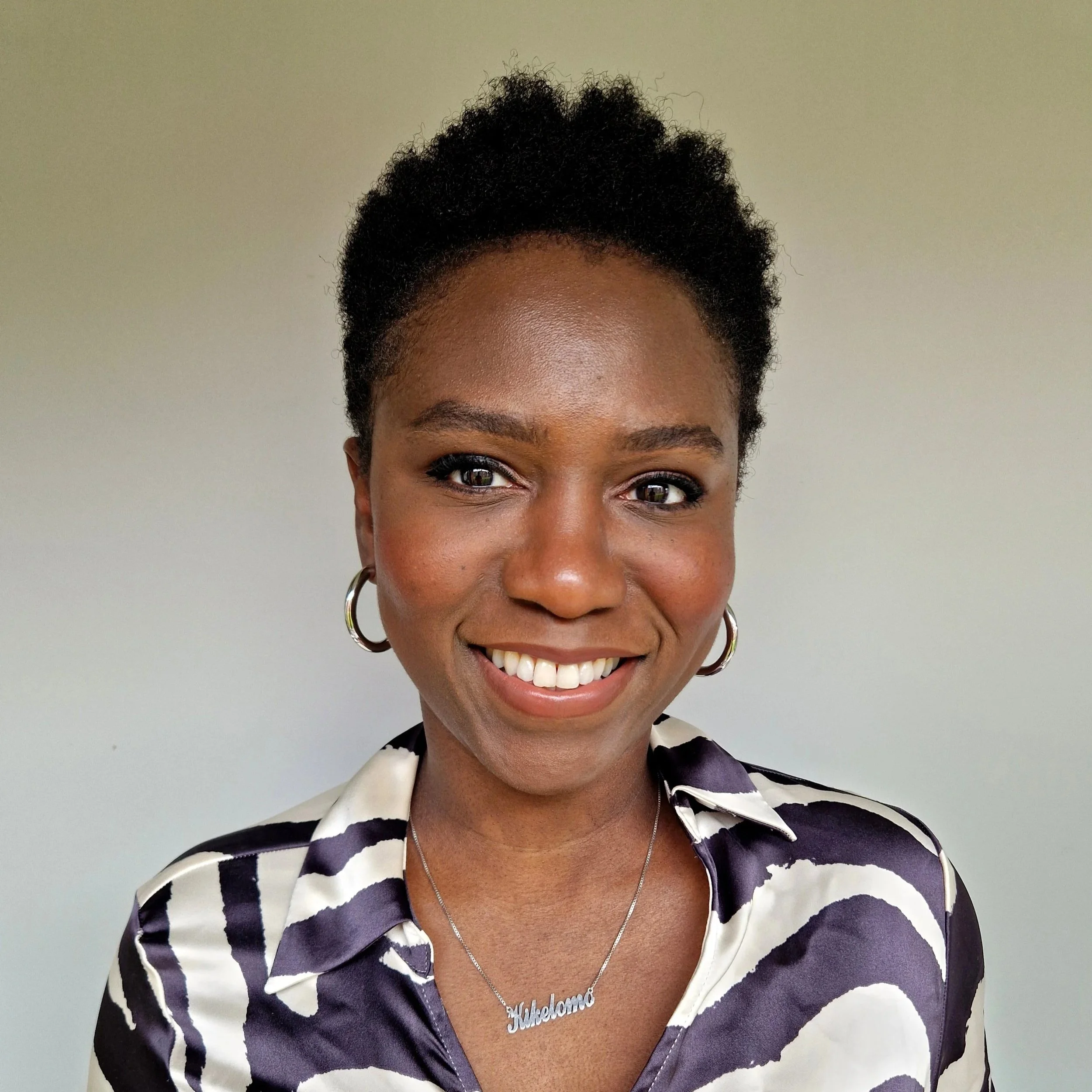 Smiling Black woman with short natural hair, hoop earrings, and a patterned blouse posing for a portrait