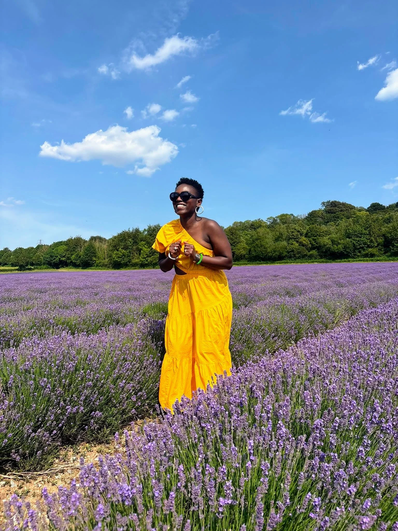 Woman in a yellow dress and sunglasses standing in a blooming lavender field under a blue sky