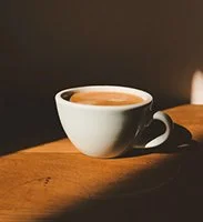 A white cup of coffee on a wooden surface with a dark background.