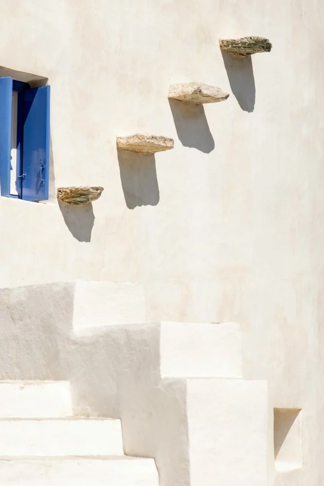 White stone staircase with four stone steps casting shadows, with a blue window on the upper left.