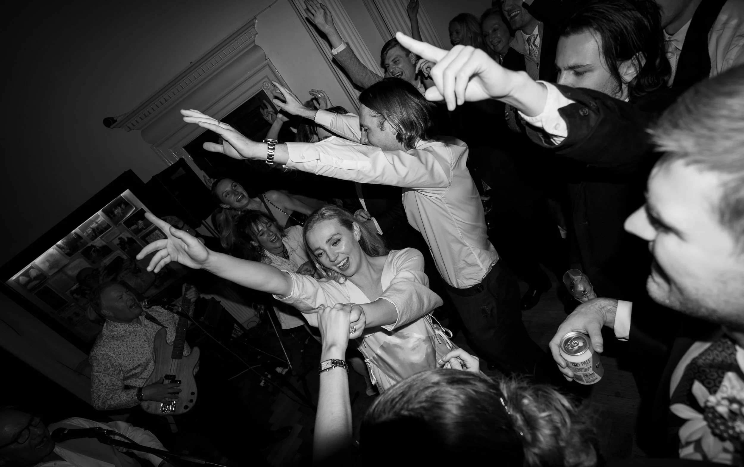 People dancing and enjoying a social event in a room, with some holding drinks, in black and white.