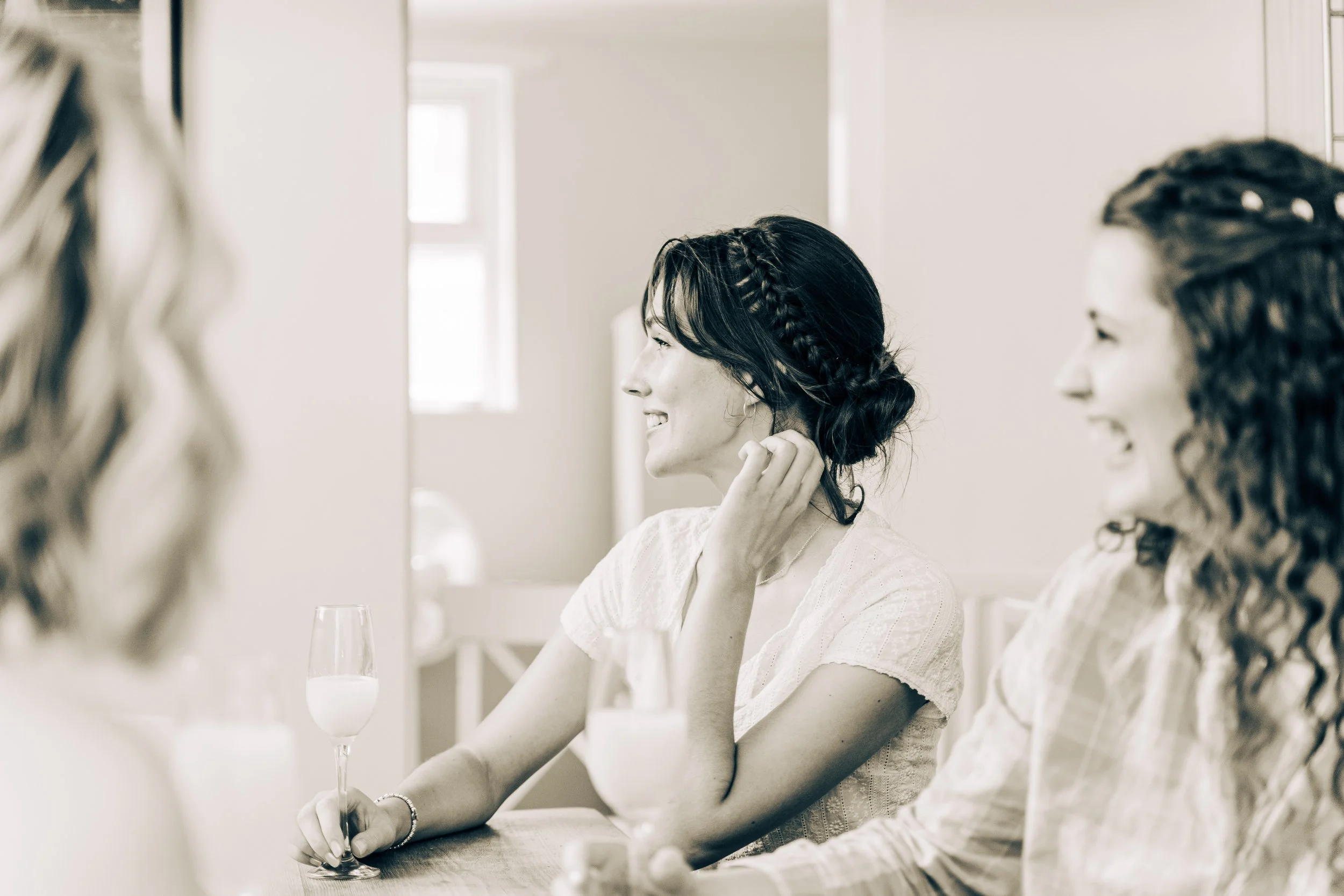 Women with curly hair sitting at a table in a well-lit room, smiling and engaging in conversation, with glasses on the table.