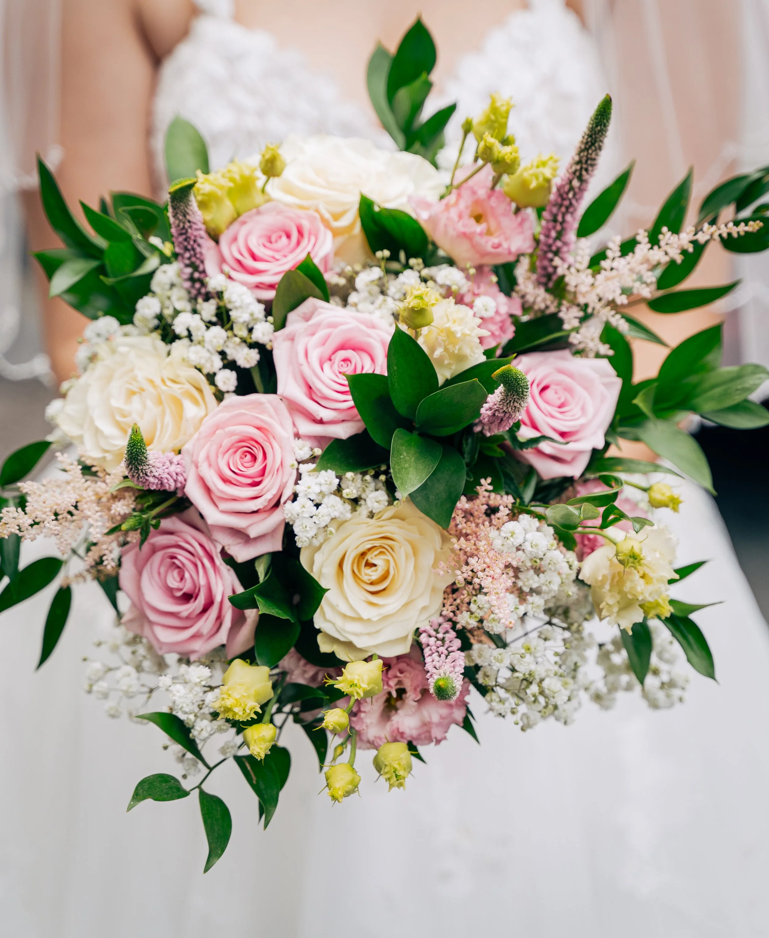 A bouquet of pink and white roses, white baby's breath, pink and white stock flowers, and green leaves.