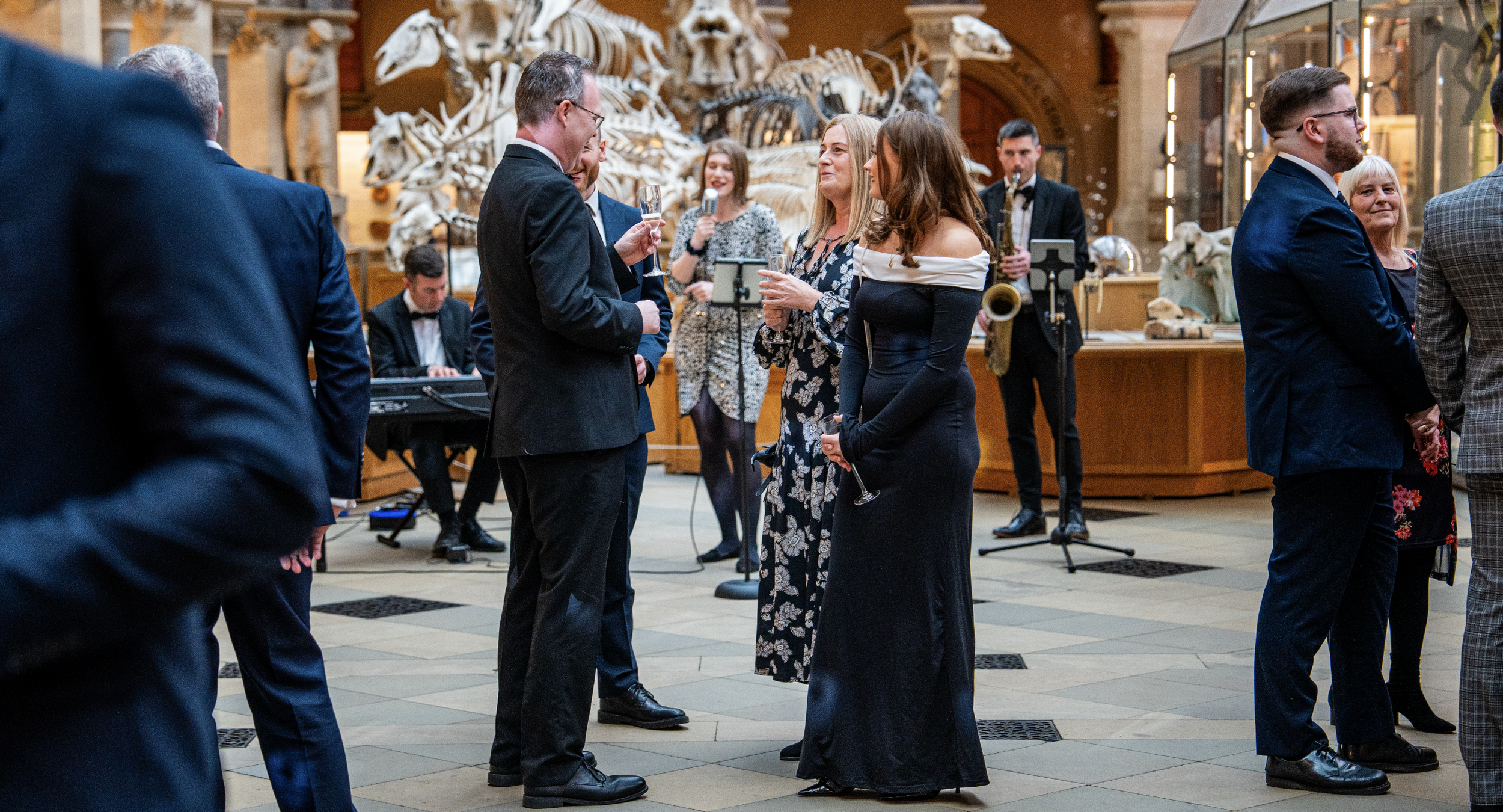 People in formal attire socializing at an event with a background of animal skeletons and museum displays.