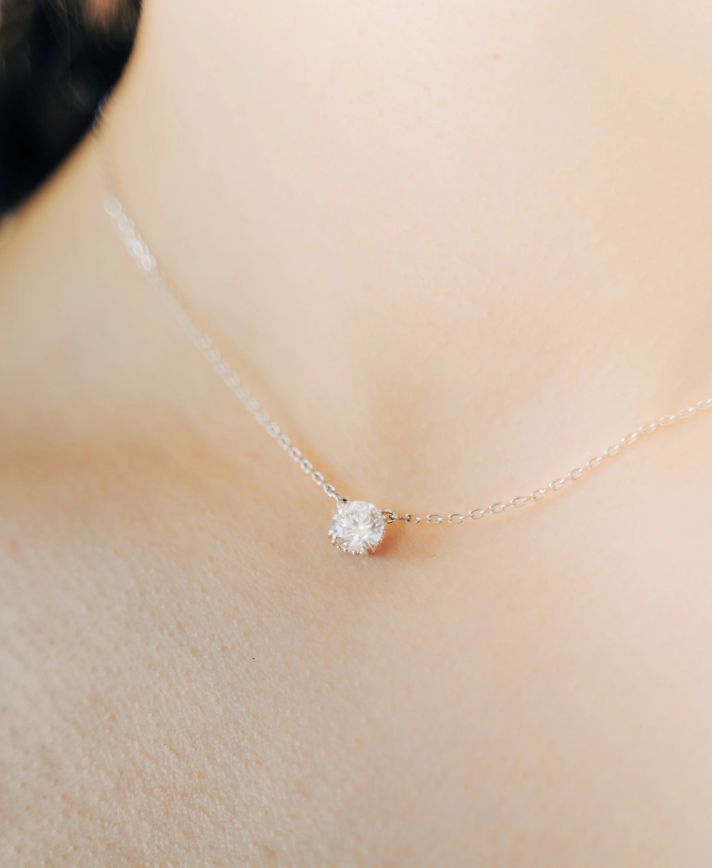 Close-up of a silver necklace with a prominent round-cut diamond pendant resting on a beige surface.