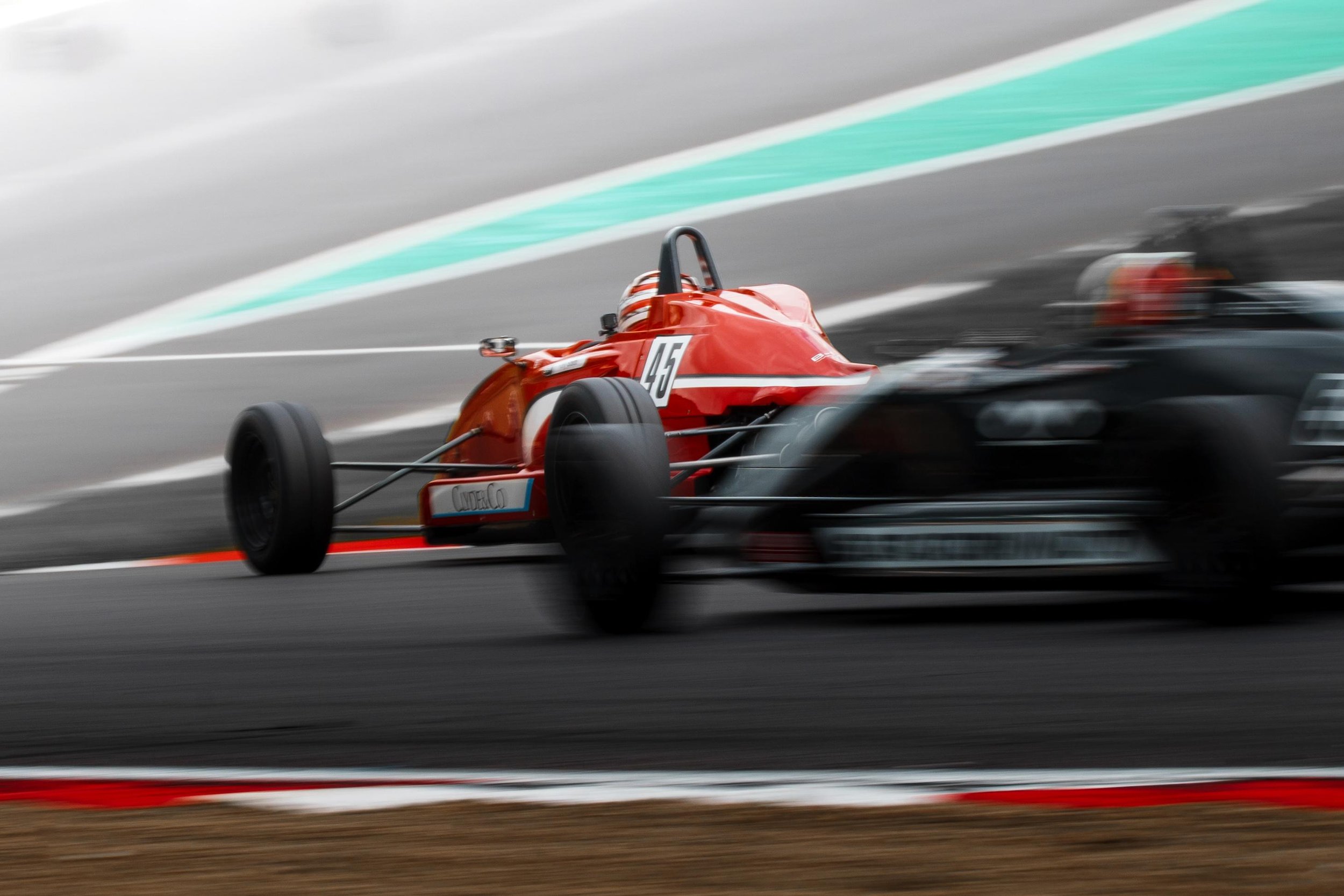 Race cars on a track, with one blurred in motion and a red and white car in focus with the number 25.