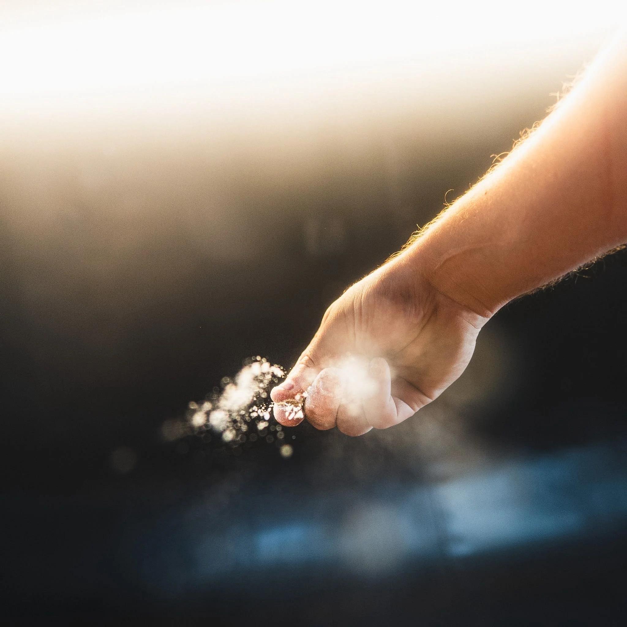 Close-up of a hand with a clenched fist releasing a cloud of white powder, with a gradient background from dark to light.
