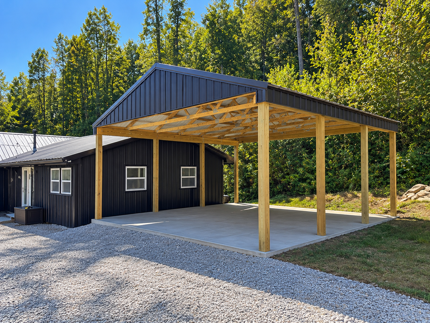 A black house with white-framed windows and a metal roof, with a wooden carport under construction attached to it, surrounded by trees.