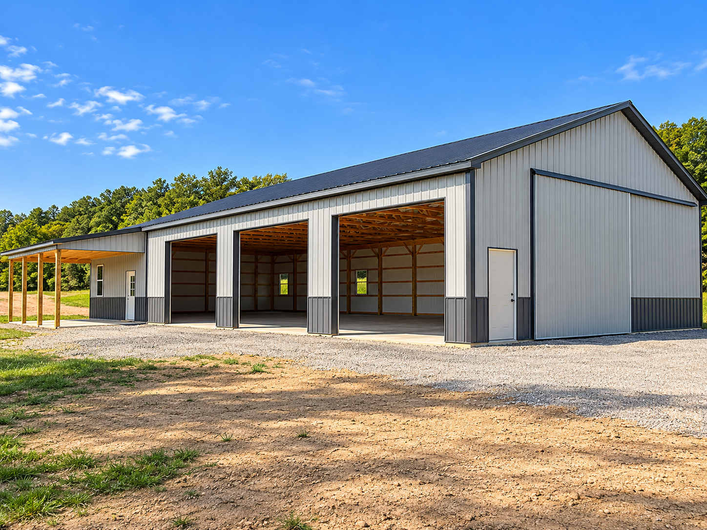 Metal building with open bays, small off-white door, and a covered extension on the left in a rural setting with trees and blue sky