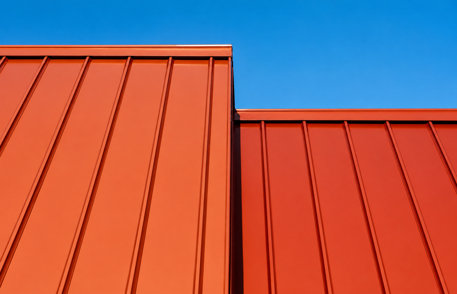 Close-up of orange metal building panels with vertical ridges against a clear blue sky.