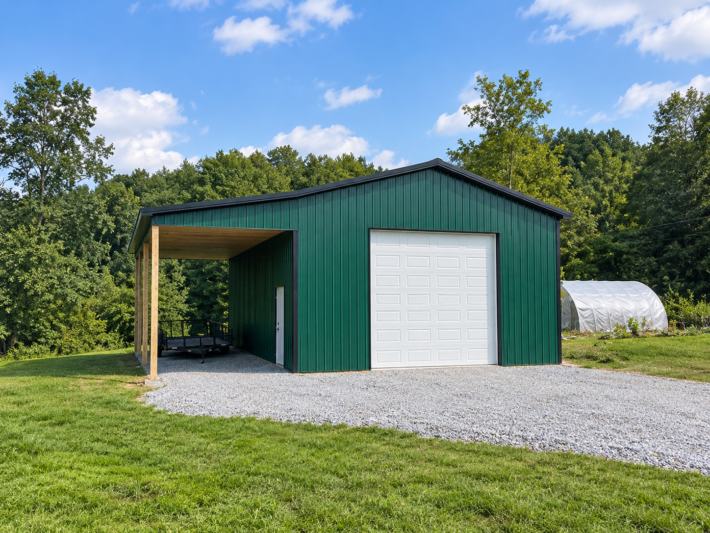 Green metal barn with a white garage door, located on a grassy area with trees and a blue sky in the background.