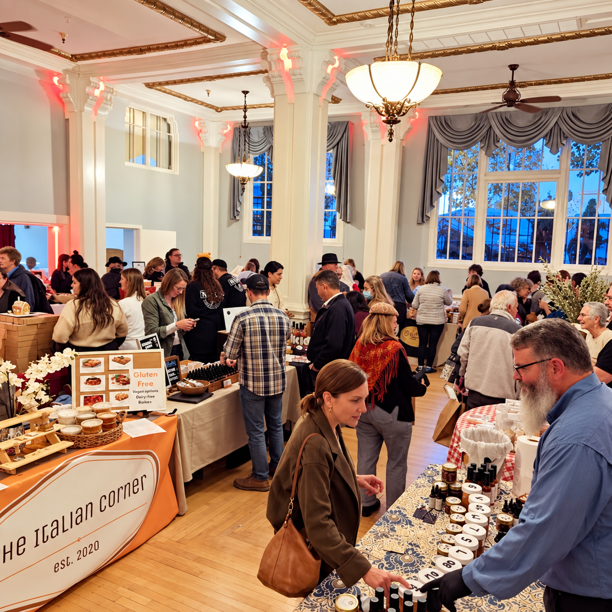 People shopping at artisan market booths inside a spacious, well-lit room with high ceilings, large windows, and decorative curtains.