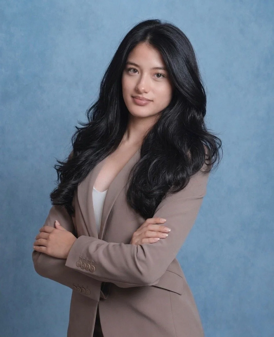 A woman with long black hair, wearing a light brown blazer with her arms crossed, standing against a blue background.