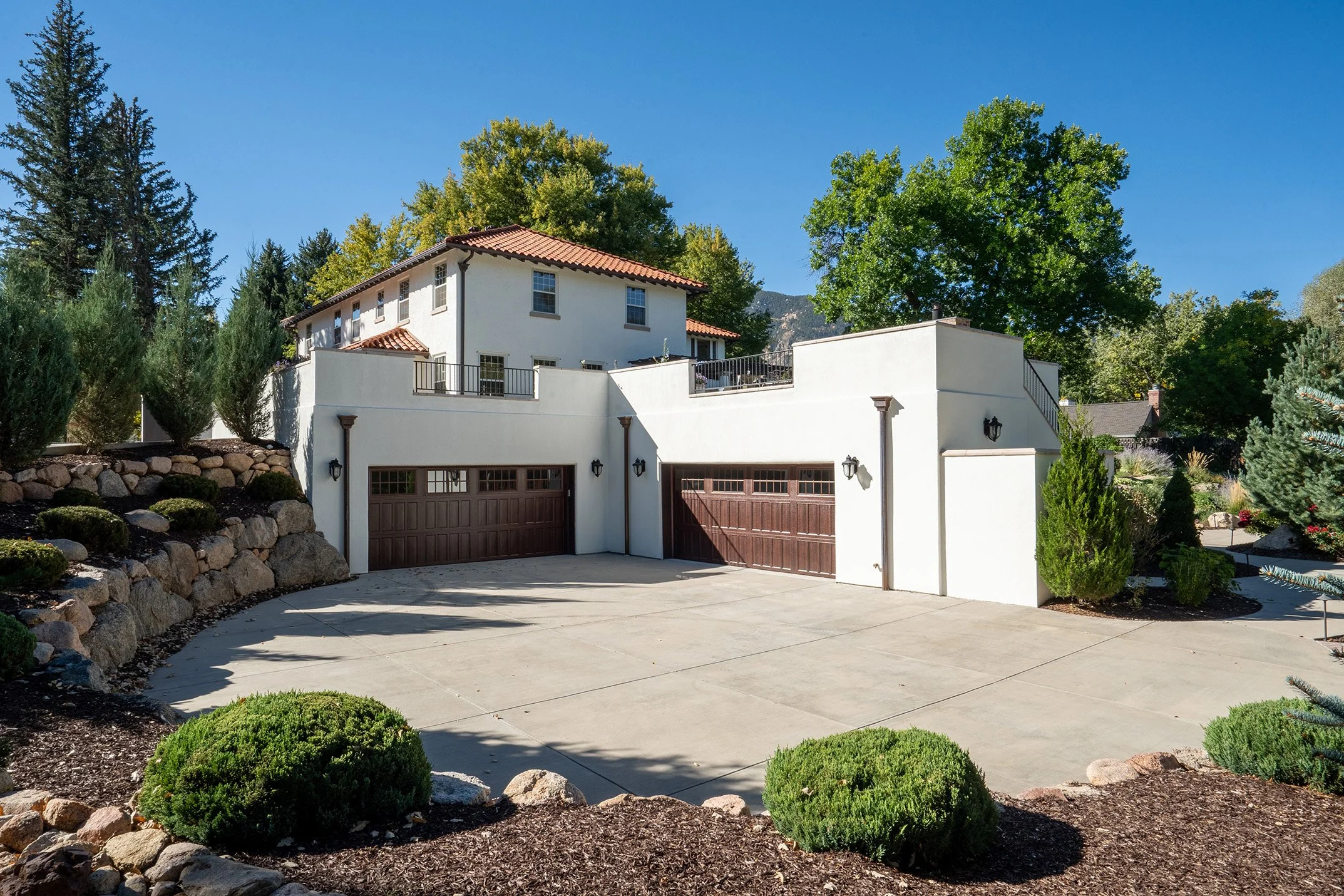 Spanish-style stucco house with red tile roof, two-car garage, landscaped yard, and mountain backdrop