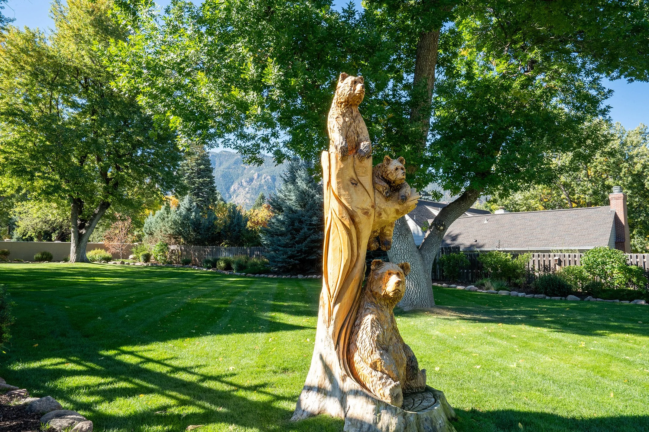 Chainsaw-carved bear family sculpture in a sunny landscaped yard with mountain views