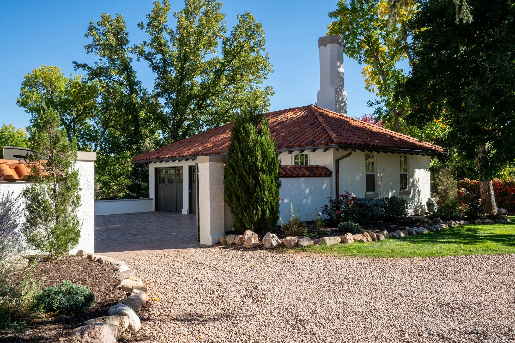 Spanish-style stucco house with a red tile roof, chimney, landscaped garden, and gravel driveway