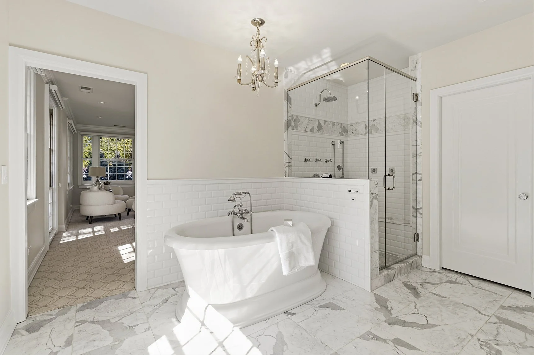 A luxurious bathroom featuring a freestanding bathtub and a glass-enclosed shower, decorated with white subway tiles and marble accents, with sunlight streaming in.