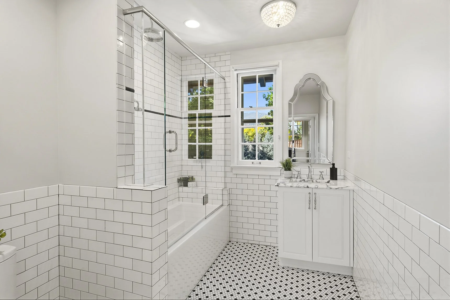 Bright white subway-tile bathroom with glass-enclosed shower, freestanding bathtub, vintage vanity, ornate mirror, and black-and-white hexagon tile floor
