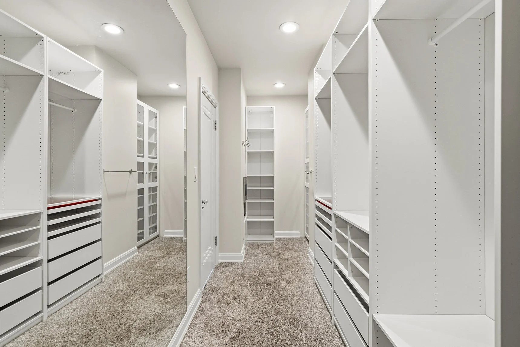 Spacious walk-in closet with white built-in shelving, drawers, clothing rods, and beige carpet